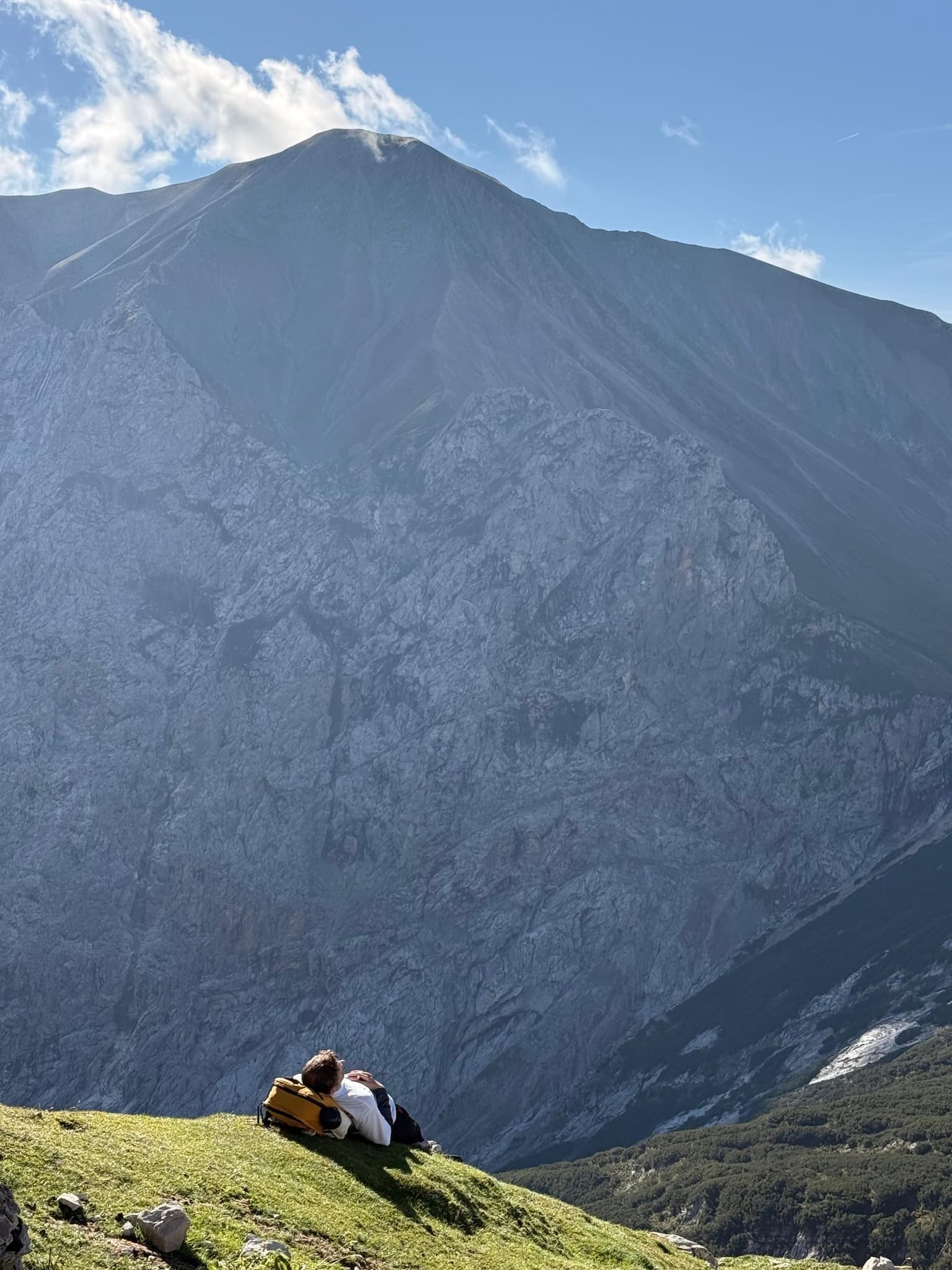cla33ic lying in an alpine meadow below a limestone summit, a yellow backpack as a pillow